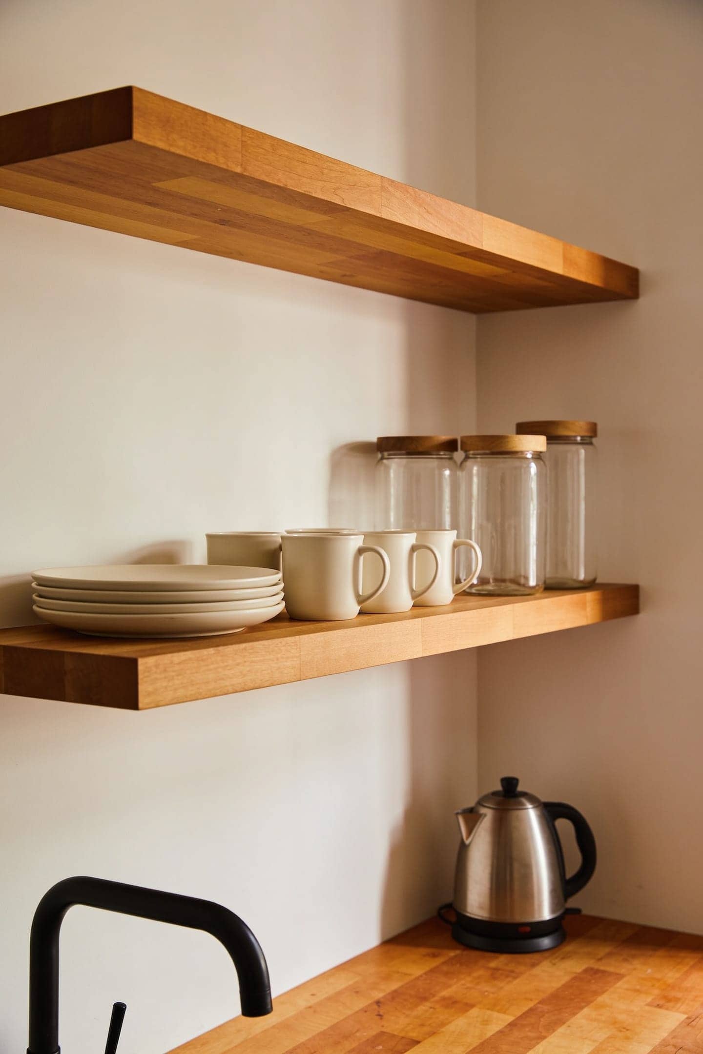 warm wood floating shelf mounted on a pale wall holding stacked plates