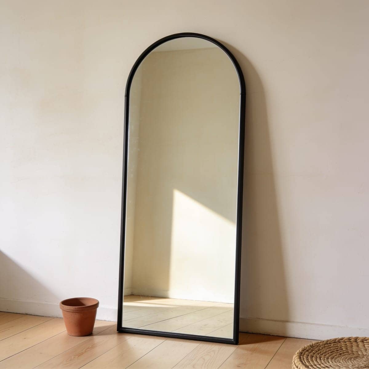 full length arched floor mirror with a slim black frame leaning against an entry wall