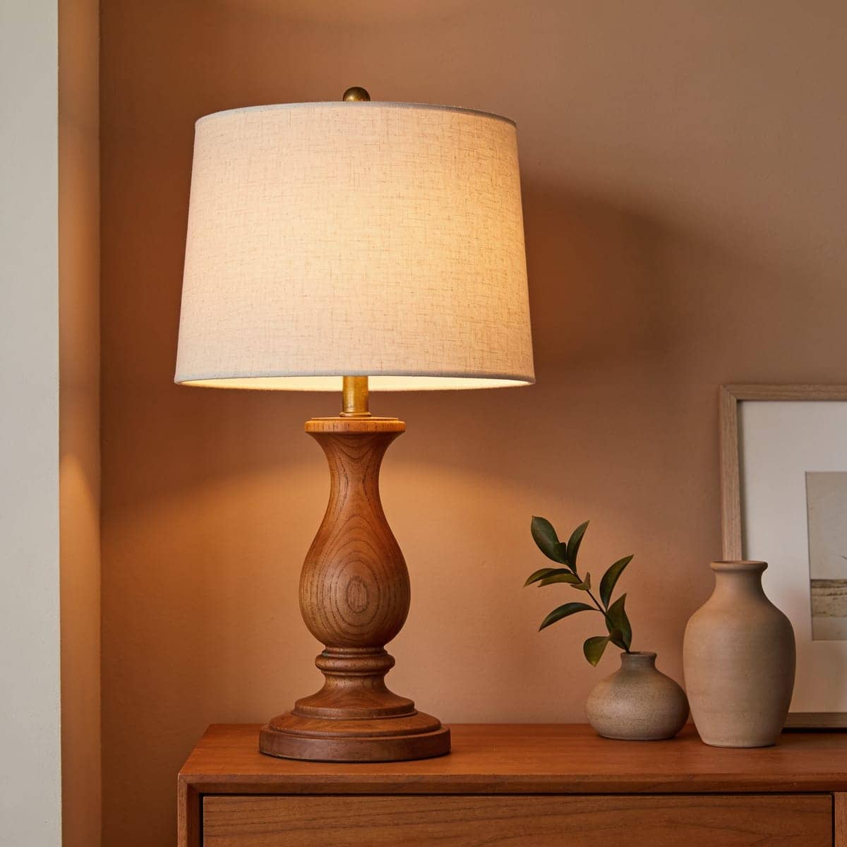 turned wood table lamp with an oatmeal linen shade in a warm bedroom
