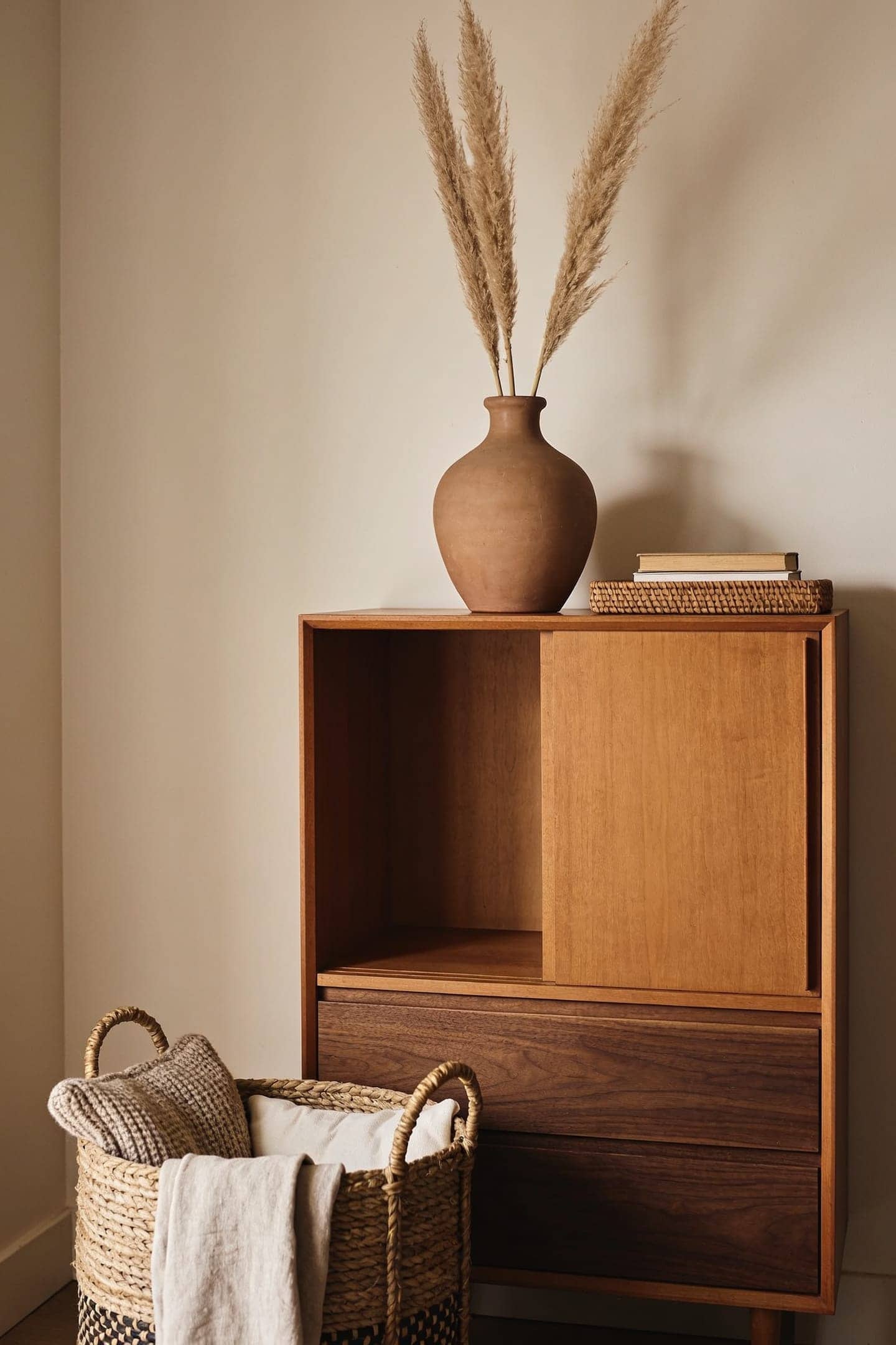 stoneware vase with dried stems and a small stack of books on a wood dresser