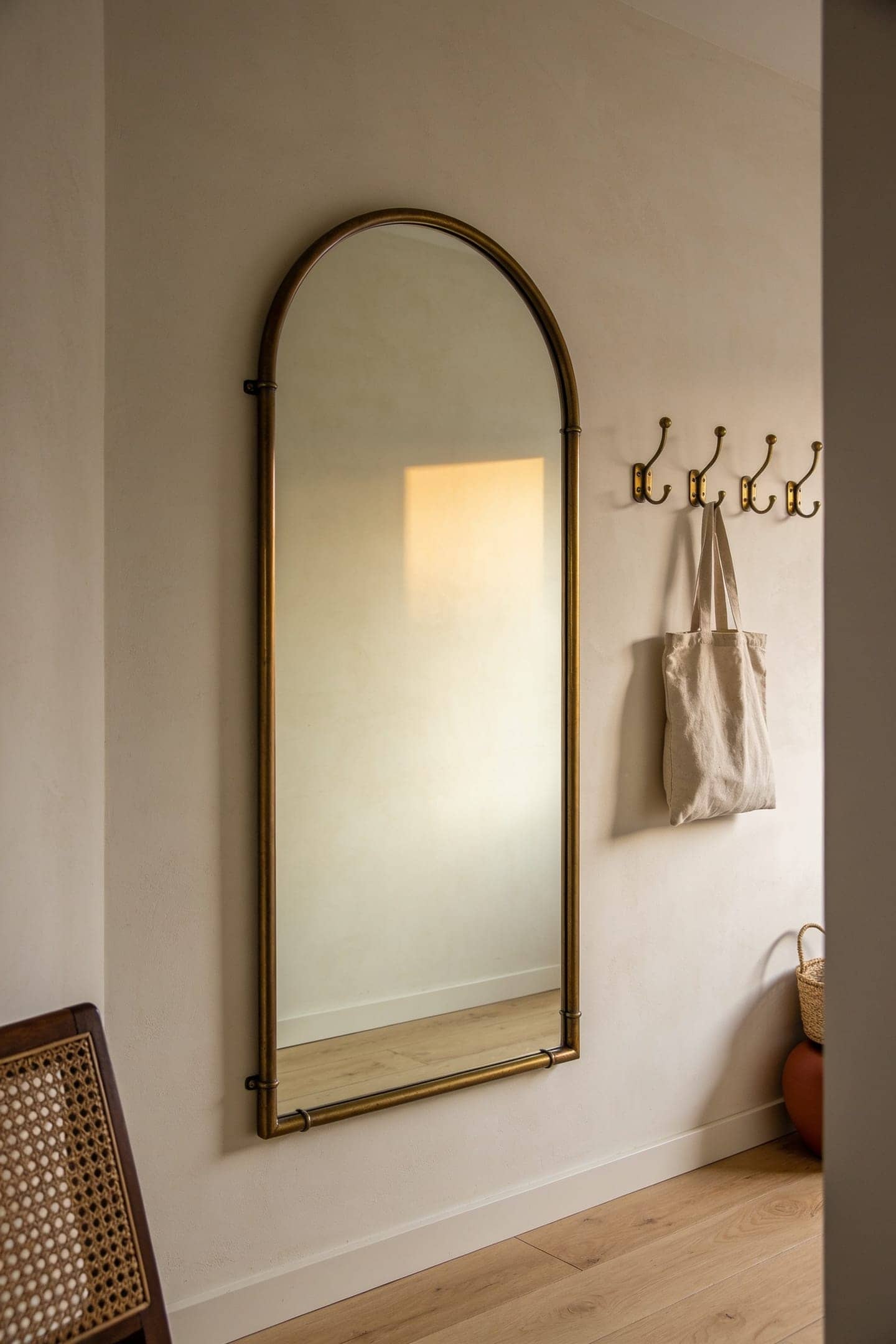 thin aged brass framed mirror above a console with matching warm brass hooks