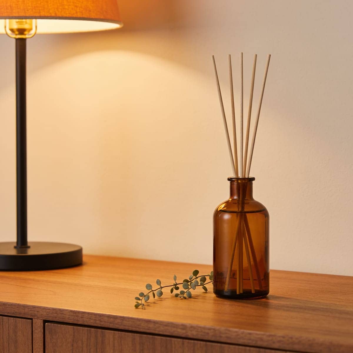 amber glass reed diffuser with rattan reeds on a shelf