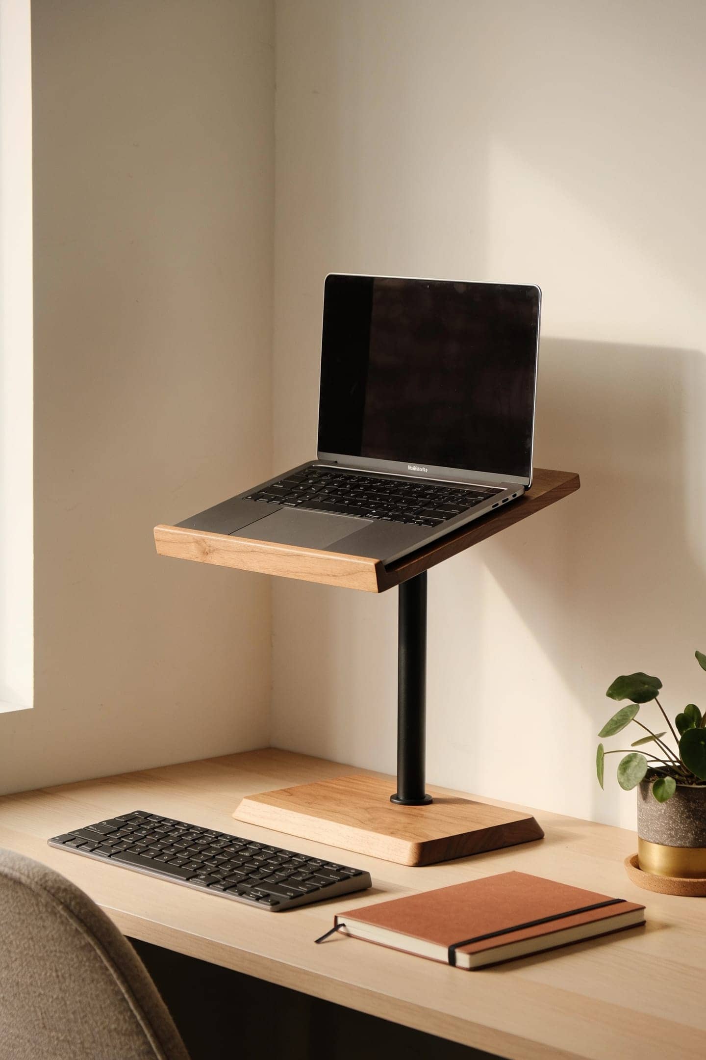 laptop lifted on a stand to eye level on a small desk next to a separate keyboard
