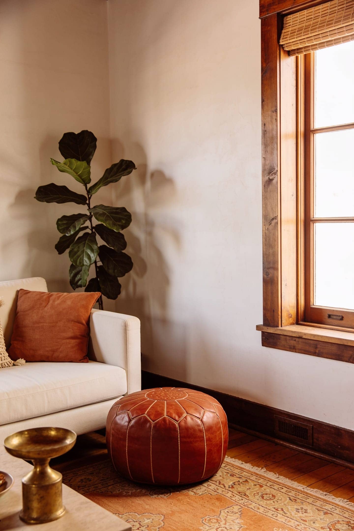 rust leather pouf next to a neutral sofa in a warm living room