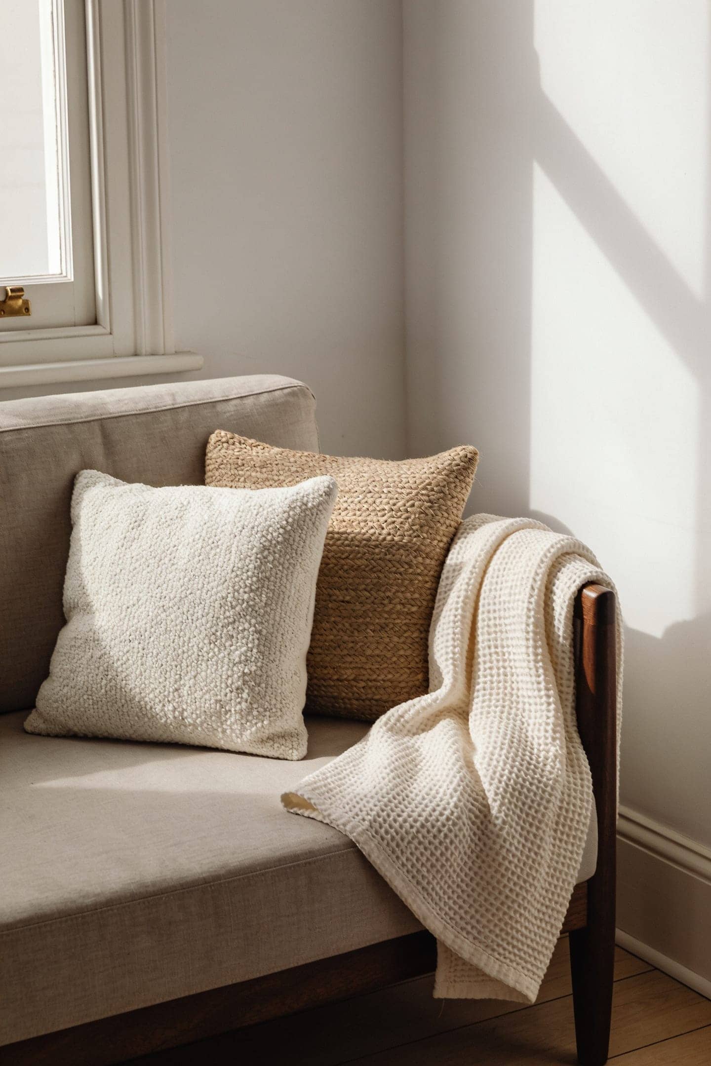 two slightly different cream cushions and an ivory throw on a sofa